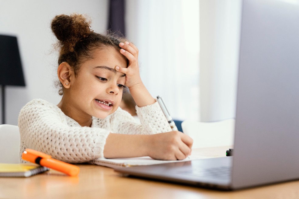 Aulas online: menina escrevendo e estudando em frente ao computador — Foto: Freepik