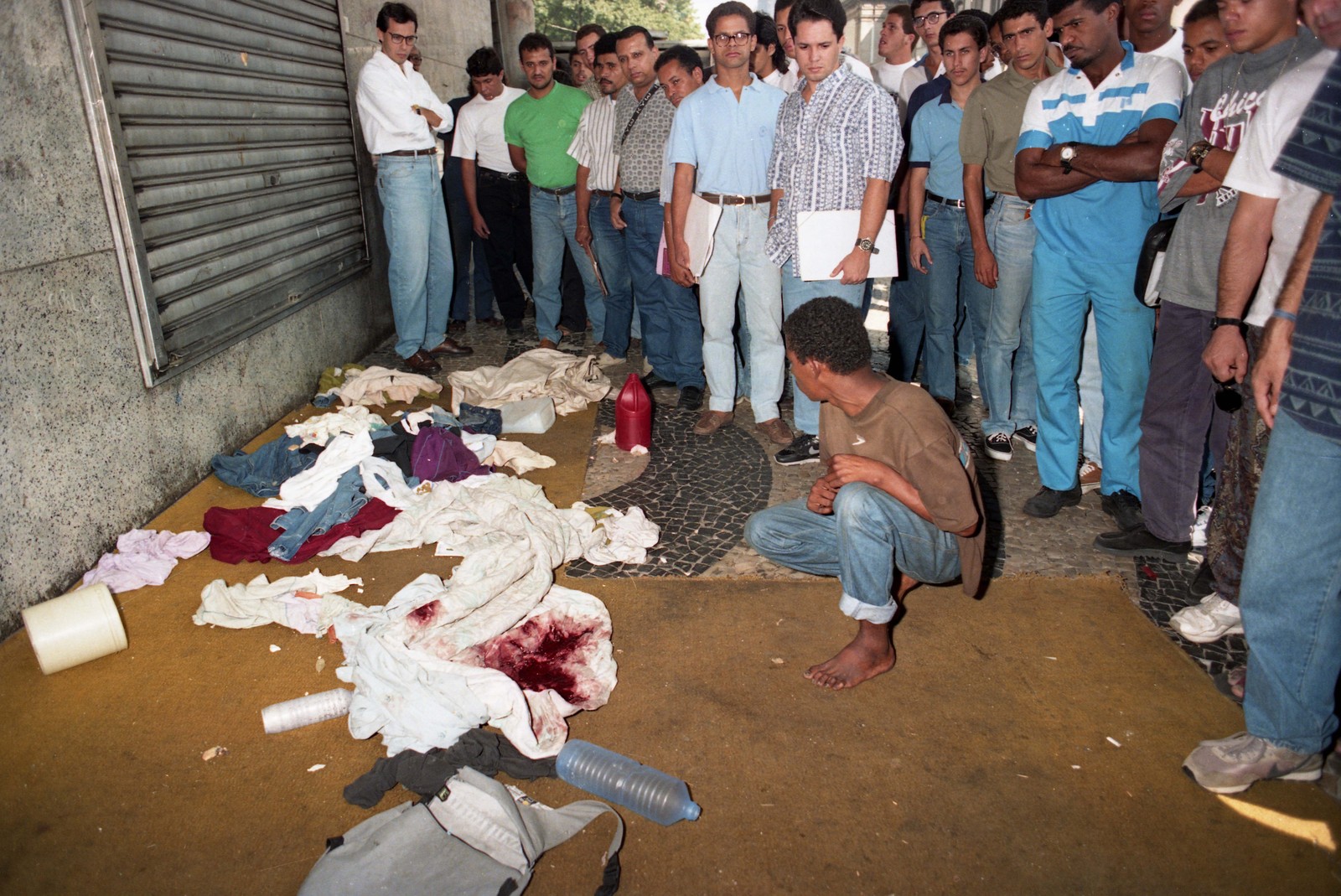 Sobrevivente observa as roupas sujas de sangue. Crime foi motivado pelo apedrejamento de um carro da PM na véspera — Foto: Ricardo Leoni / Agência O Globo