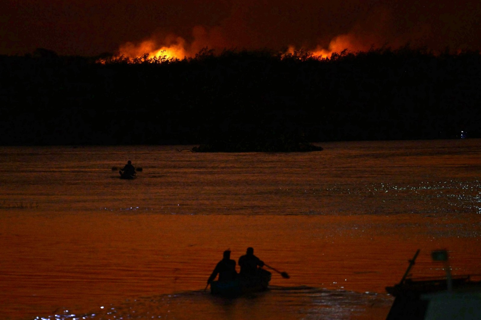 Moradores de Corumbá em barco no Rio Paraguai com o Pananal em chamas, ao fundo — Foto: Pablo PORCIUNCULA / AFP