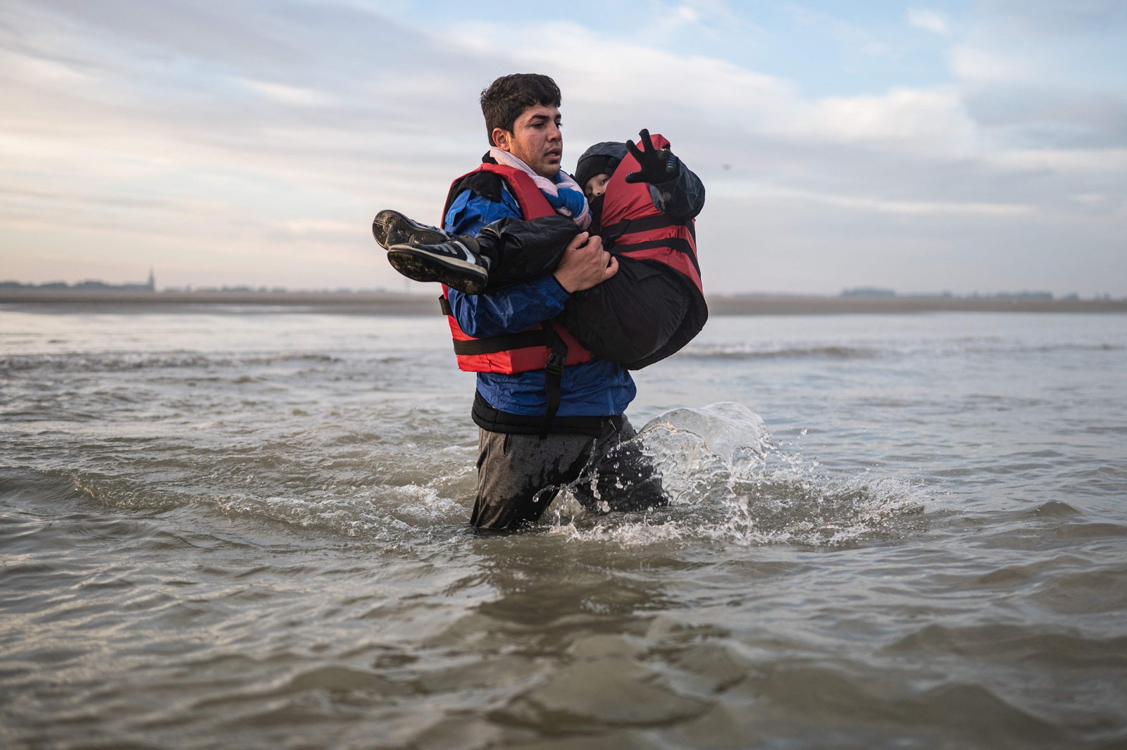 Migrante carrega uma criança enquanto corre para embarcar no barco de um contrabandista na praia de Gravelines, perto de Dunquerque, norte da França — Foto: SAMEER AL-DOUMY/AFP