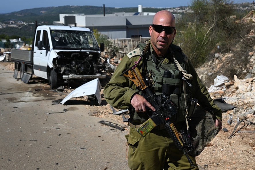 Soldado israelense fala ao lado de um carro danificado perto da fronteira com o Líbano