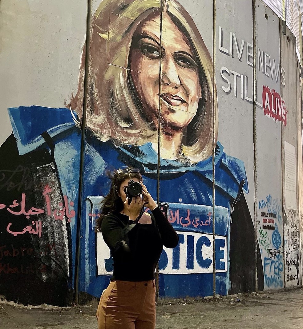 Leali Shalabi no muro que separa a Cisjordânia de Israel. Atrás, uma homenagem à jornalista da al-Jazeera Shireen Abu Akleh, morta durante um conflito — Foto: Reprodução/Instagram