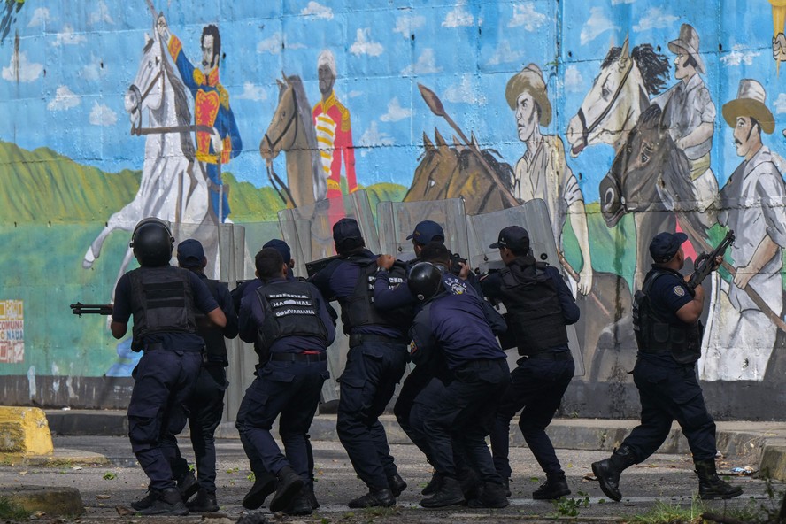 Com mural de Simon Bolívar ao fundo, policiais enfrentam manifestantes em rua de Caracas