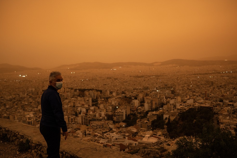 Um homem usando uma máscara facial olha para a cidade de Atenas da colina Tourkovounia, após ventos do sul carregarem ondas de poeira do Saara para a cidade — Foto: Angelos Tzortzinis/ AFP