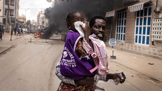 Homem corre com sua filha enquanto ela cobre o nariz do gás lacrimogêneo em Dacar, palco de protestos durante julgamento de líder da oposição preso — Foto: JOHN WESSELS/AFP