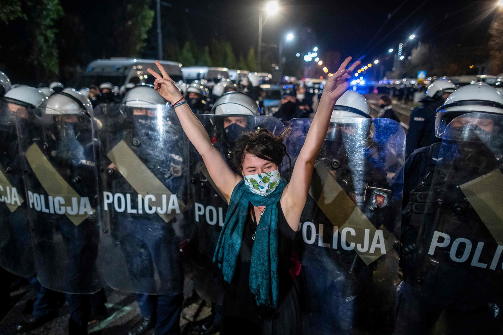 Manifestante mostra o sinal V em frente a uma linha da tropa de choque que guarda a casa de Jaroslaw Kaczynski, líder do partido governista da Lei e Justiça (PIS), durante uma manifestação contra uma decisão do Tribunal Constitucional sobre revogar interrupção da gravidez por má-formação, em Varsóvia, PolôniaAFP