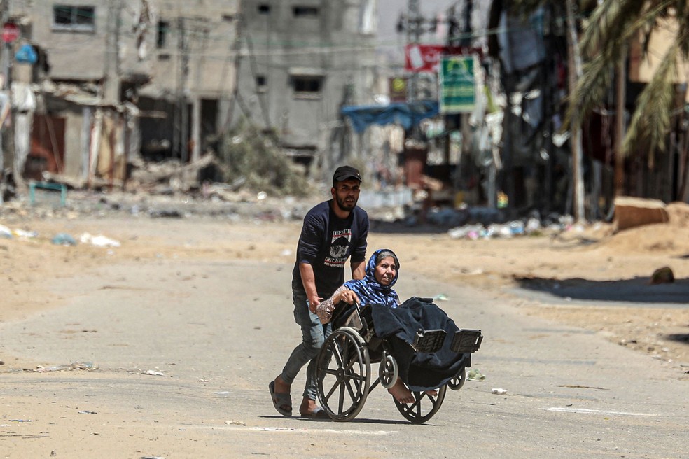 Um homem empurra uma mulher idosa em uma cadeira de rodas enquanto palestinos fogem de suas casas no campo de refugiados de Nuseirat, no centro da Faixa de Gaza. — Foto: AFP