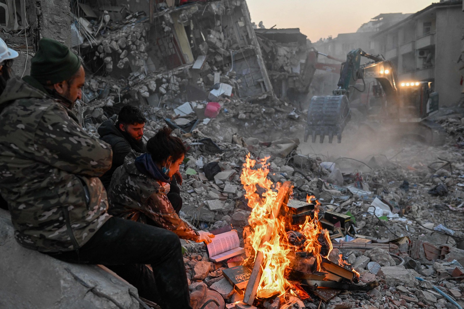 Sobreviventes queimam livros para se manter aquecidos à espera de resgate nos escombros em Hatay, Turquia — Foto: BULENT KILIC/AFP