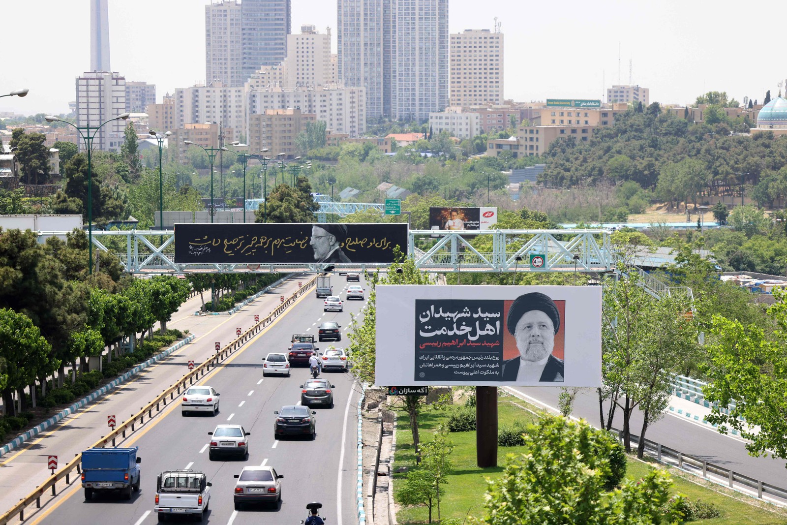 O tráfego passa por faixas com retratos do falecido presidente do Irã, Ebrahim Raisi, no centro de Teerã — Foto: ATTA KENARE / AFP