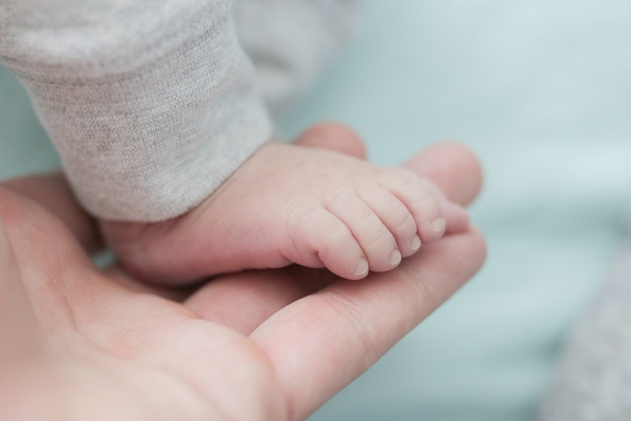 Imagem ilustrativa do pé de um bebê sobre a mão de um adulto