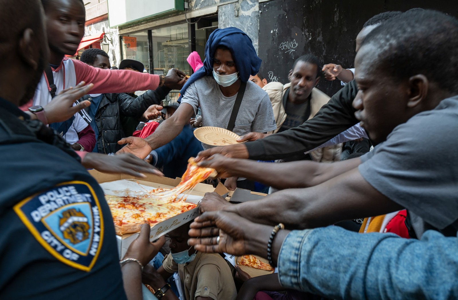 Um policial distribui pizza a dezenas de imigrantes recém-chegados à cidade de Nova York enquanto acampam do lado de fora do Hotel Roosevelt — Foto: SPENCER PLATT / Getty Images via AFP