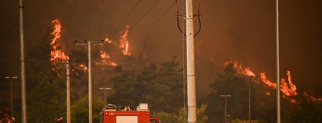 Um veículo de combate a incêndios circula em uma estrada durante um incêndio florestal em Chasia, nos arredores de Atenas — Foto: Angelos Tzortzinis / AFP