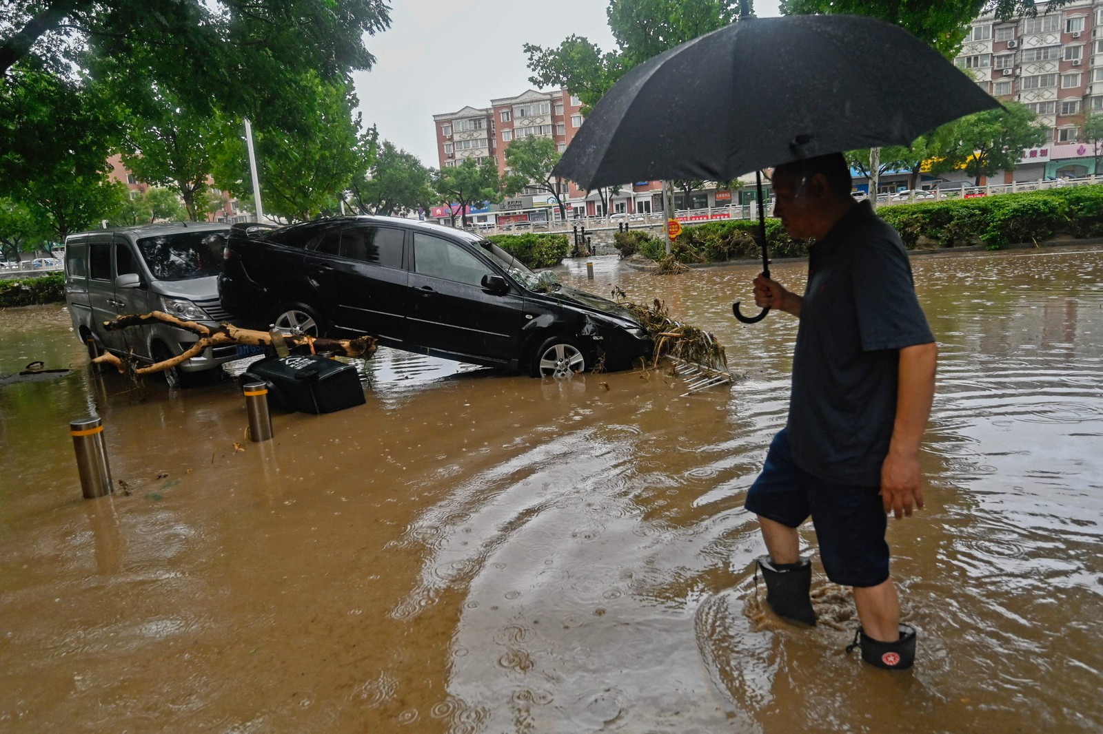 Homem passa por um carro danificado ao longo de uma rua inundada, após fortes chuvas no distrito de Mentougou, em Pequim — Foto: Pedro Pardo / AFP