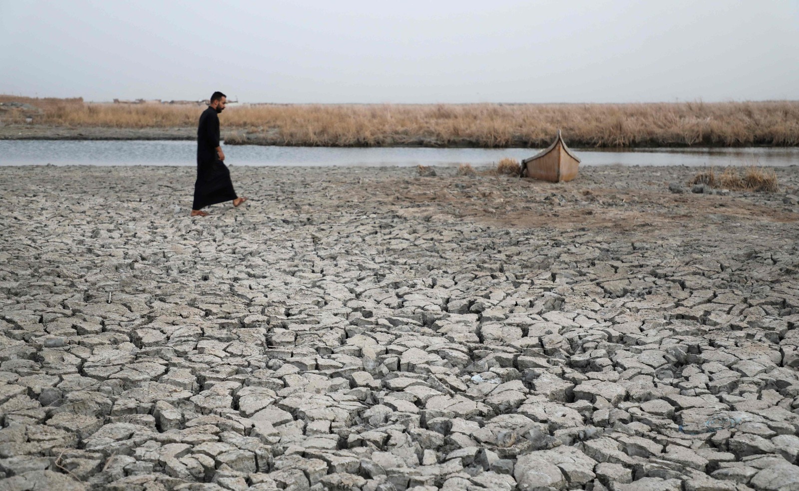 Homem se aproxima de um barco preso na margem seca de um canal em Umm El Wadaa, sudeste da cidade iraquiana de Nasiriyah, no sul da província de Dhi Qar, em 16 de agosto de 2022 — Foto: Assad Niazi / AFP