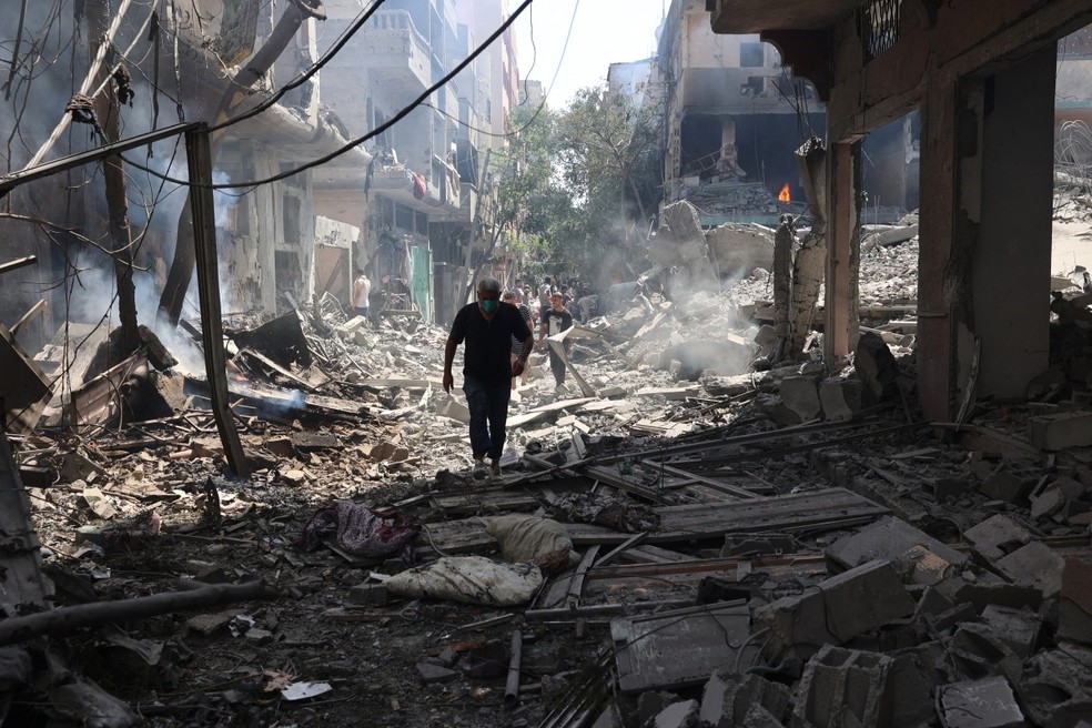 homem palestino caminha sobre os escombros de edifícios destruídos após uma operação das Forças Especiais Israelenses no campo de Nuseirat, no centro da Faixa de Gaza. — Foto: EYAD BABA/AFP