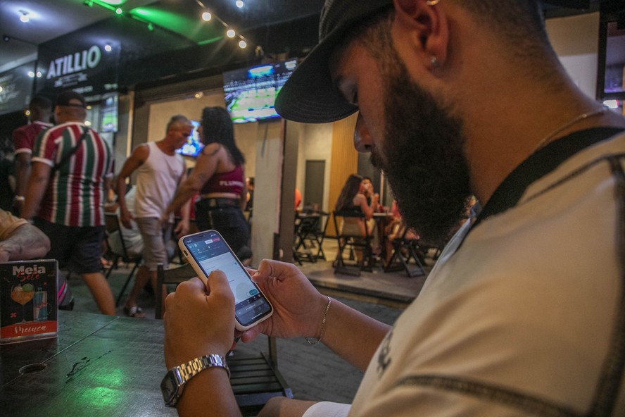 Torcedor acompanha jogo em bar de olho nas apostas na tela do celular