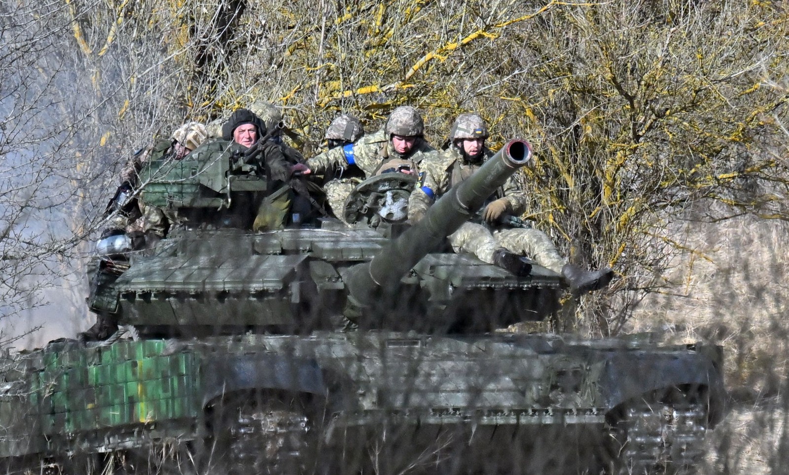 Perto dali, um tanque carregando soldados ucranianos se move por uma planície na orla da floresta, rolando sobre trechos de neve derretida — Foto: Sergei Supinsky / AFP