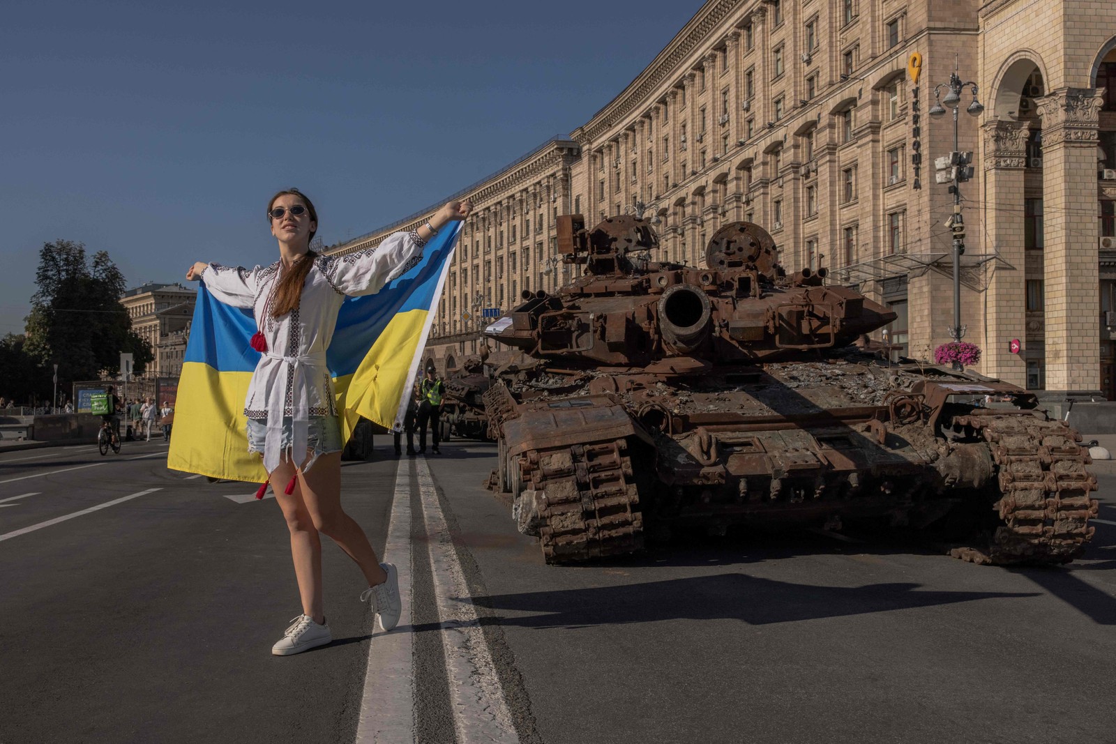 Mulher posa para fotos segurando a bandeira ucraniana ao lado de veículos militares russos destruídos em Kiev — Foto: Roman Pilipey / AFP