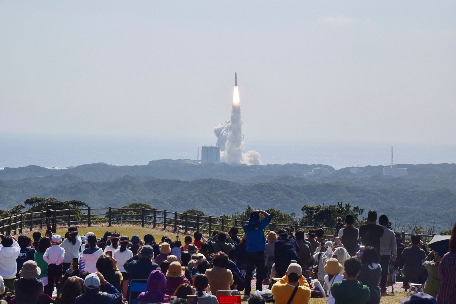 Pessoas assistem ao lançamento do foguete japonês de última geração H3, que fracassou por não ignição do motor de segunda fase e foi abatido com satélites que transportava — Foto: JIJI Press/AFP