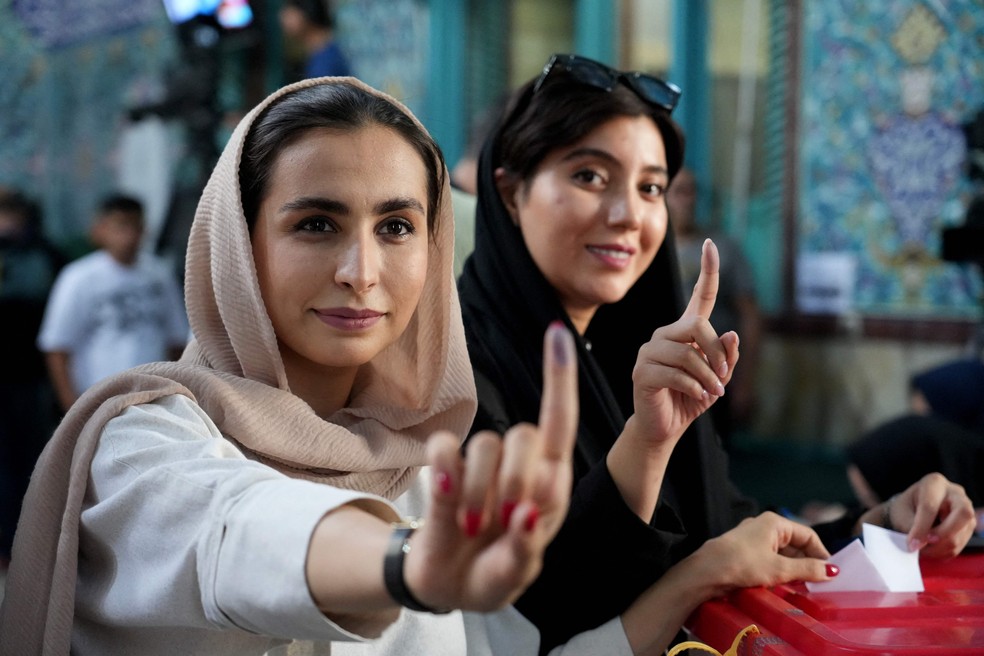 Iranianas mostram os dedos marcados com tinta depois de votarem no segundo turno da eleição presidencial no Irã — Foto: RAHEB HOMAVANDI / AFP