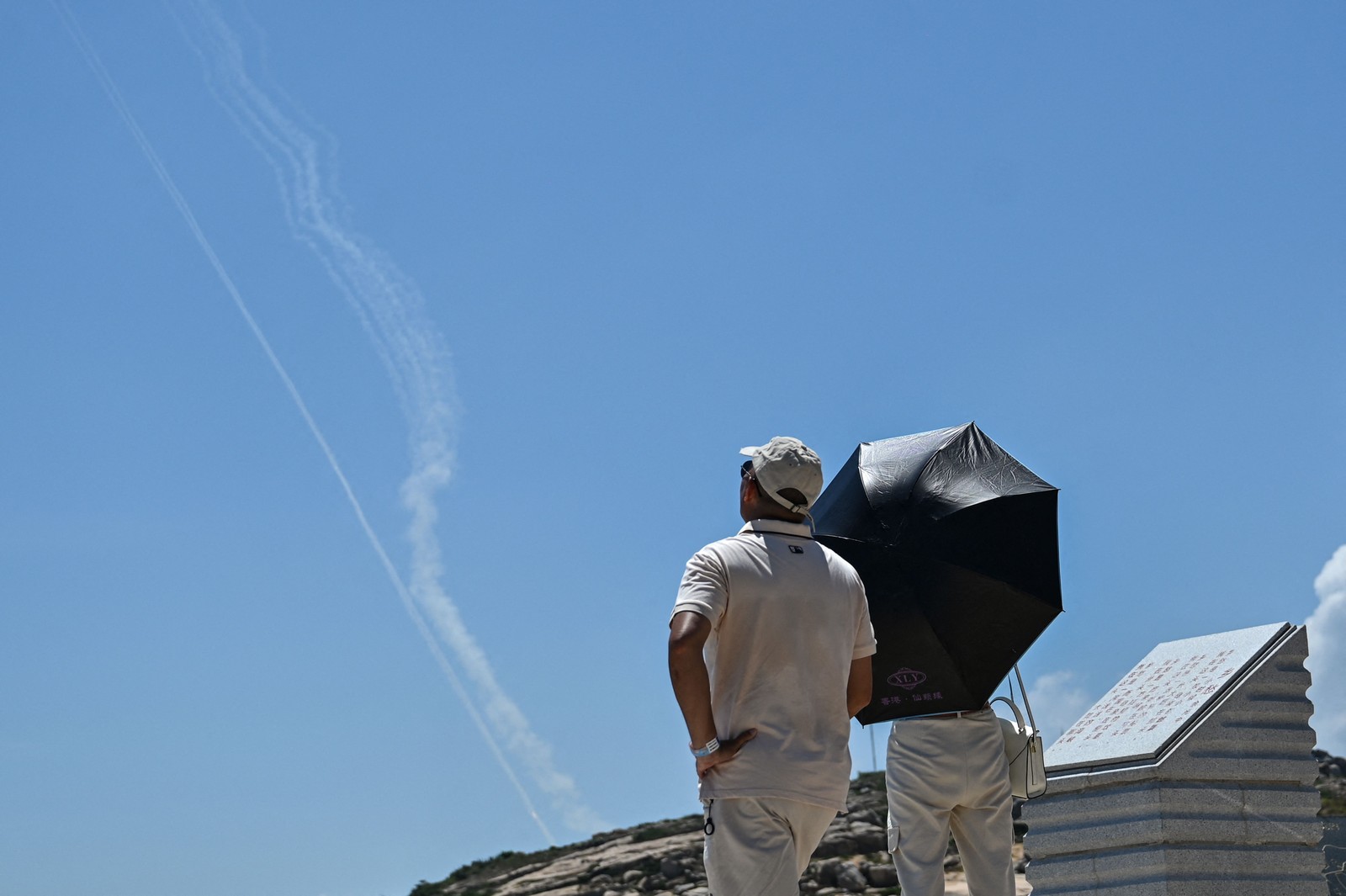 Turistas observam trilho de fumaça de projétil lançado durante exercício militar chinês na ilha de Taiwan — Foto: Hector Retamal / AFP