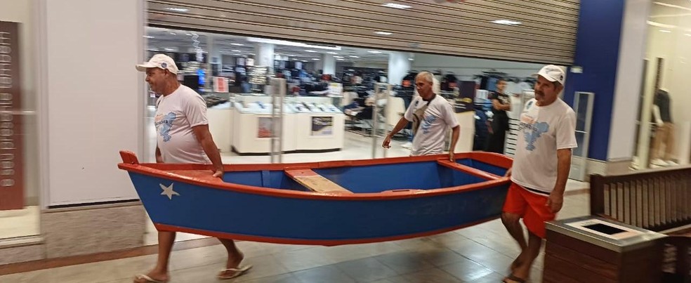 Pescadores, responsáveis pela limpeza da Baía de Guanabara, chegando  ao shopping com o barco que será usado na exposição — Foto: Divulgação