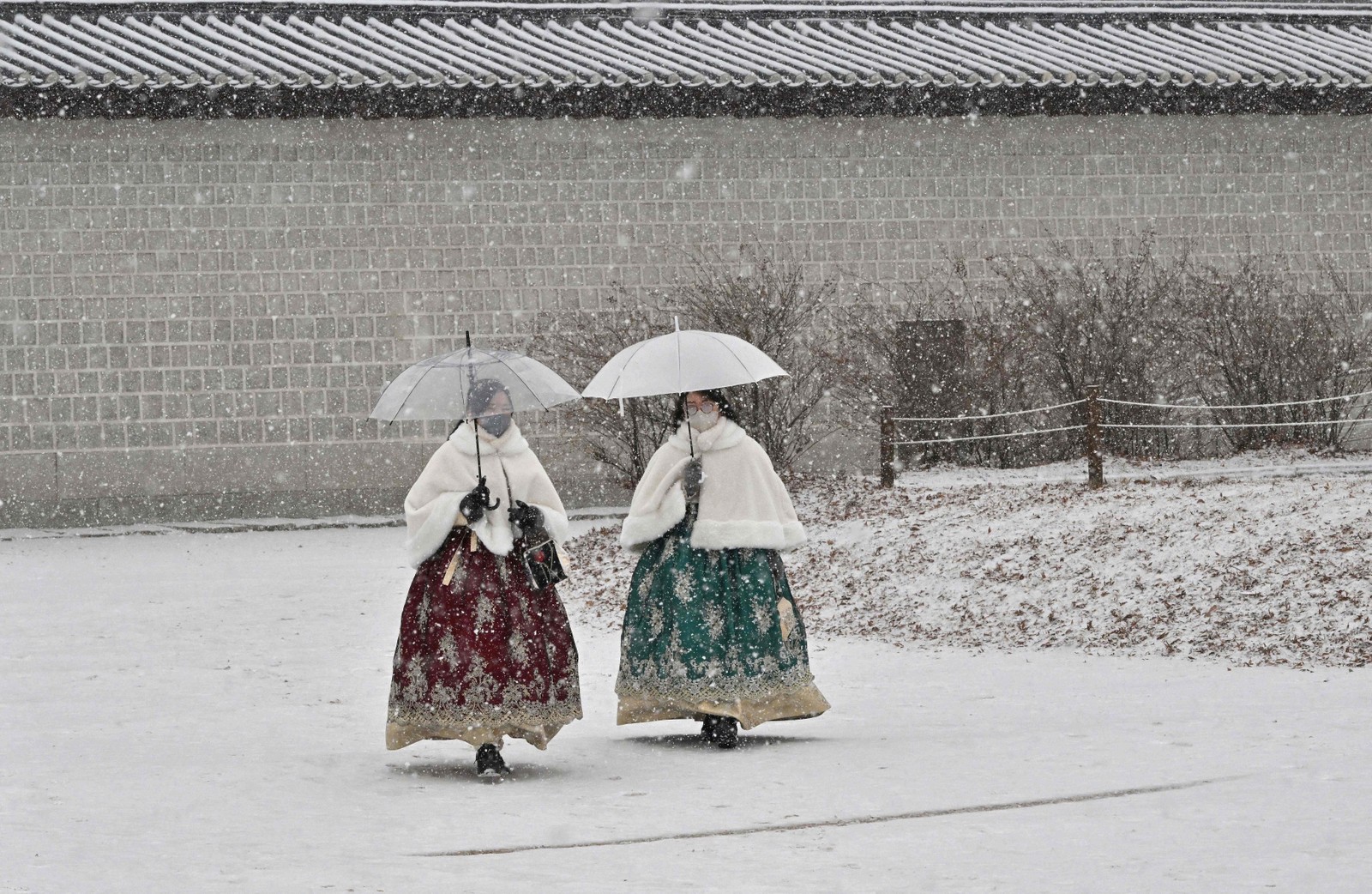 Visitantes vestindo trajes tradicionais hanbok caminham pelo palácio Gyeongbokgung durante a nevasca no centro de Seul, Coreia do Sul — Foto: JUNG YEON-JE/AFP