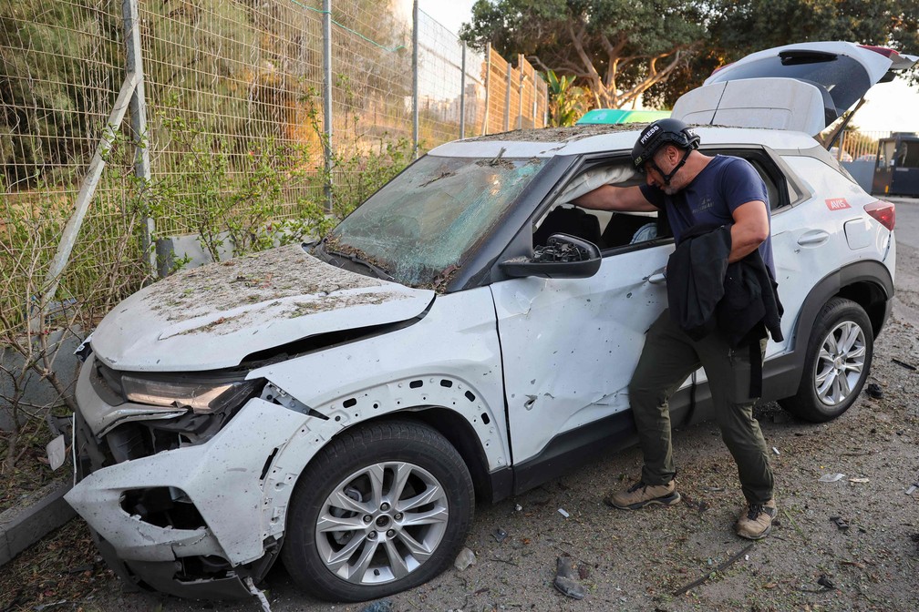 Um jornalista italiano verifica seu carro, danificado por um ataque de foguete da Faixa de Gaza, na cidade de Ashkelon, no sul de Israel — Foto: JACK GUEZ/AFP