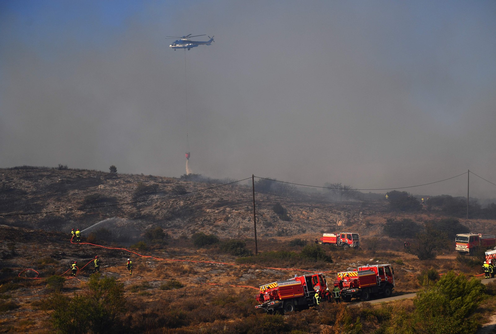 Helicóptero reforça o trabalho dos que bombeiros combatem incêndio florestal em Tarascon, sudeste da França  — Foto: CLEMENT MAHOUDEAU / AFP