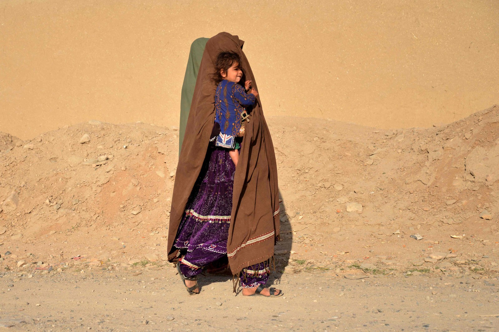 Mulher carrega criança ao longo de uma estrada no distrito de Zhari, na província de Kandahar, Afeganistão — Foto: SANAULLAH SEIAM/AFP