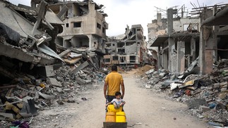 Palestinos em meio a edifícios destruídos em Khan Yunis, no sul da Faixa de Gaza — Foto: AFP