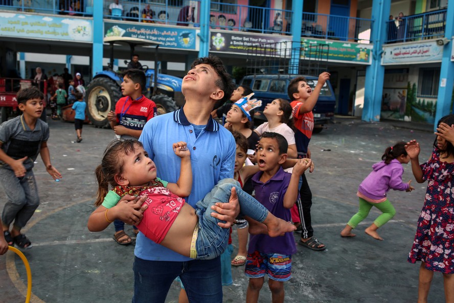 Crianças palestinas que buscam abrigo em uma escola na Cidade de Gaza olham para o céu enquanto jatos israelenses sobrevoam, uma das primeiras respostas de Israel ao ataque terrorista do Hamas.