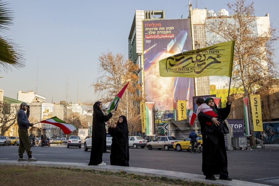 Iranianos pró-governo se reúnem perto de uma faixa que avisa os inimigos do Irã, em farsi e em hebraico, para 'prepararem seus caixões', em Teerã