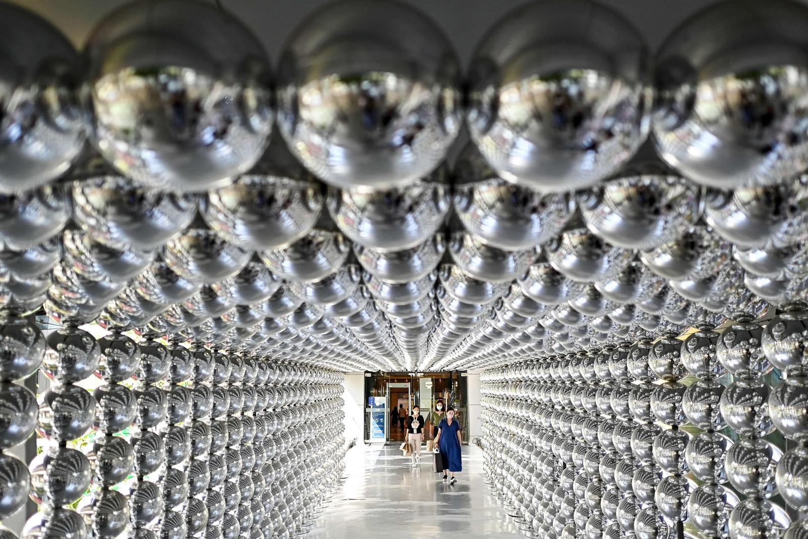 Mulheres passam por uma decoração feita de bolas reflexivas do lado de fora de um shopping center em Bangcoc.  — Foto: MANAN VATSYAYANA / AFP