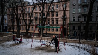 Uma mulher balança seu filho em um parquinho parcialmente destruído por um ataque com mísseis ocorrido em outubro de 2022, no centro de Kiev — Foto: Dimitar DILKOFF / AFP - 13/02/2023