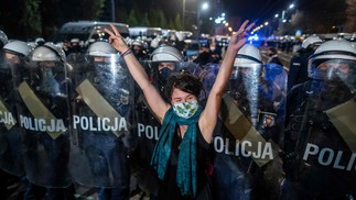 Manifestante mostra o sinal V em frente a uma linha da tropa de choque que guarda a casa de Jaroslaw Kaczynski, líder do partido governista da Lei e Justiça (PIS), durante uma manifestação contra uma decisão do Tribunal Constitucional sobre revogar interrupção da gravidez por má-formação, em Varsóvia, PolôniaAFP