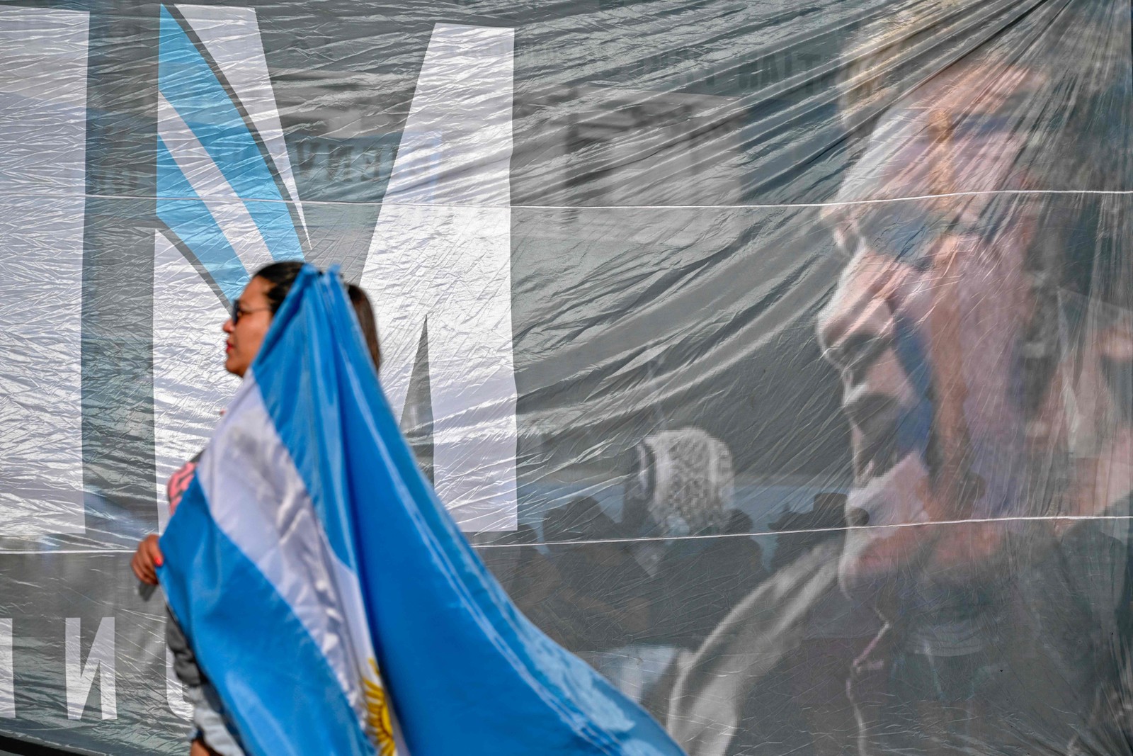 Apoiador de Milei passa em frente a telão com o rosto do presidente eleito da Argentina — Foto: Luis ROBAYO / AFP