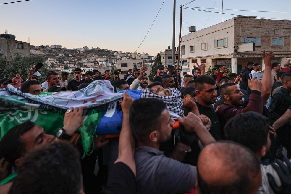 População carrega o corpo de um dos atiradores que matou quatro israelenses na Cisjordânia — Foto: JAAFAR ASHTIYEH/AFP