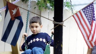 Elián González, em abril de 2000, balança entre as bandeiras de Cuba e dos EUA do lado de fora da residência de seu tio-avô,  na seção Little Havana de Miami, Flórida — Foto: Meredith DAVENPORT / AFP