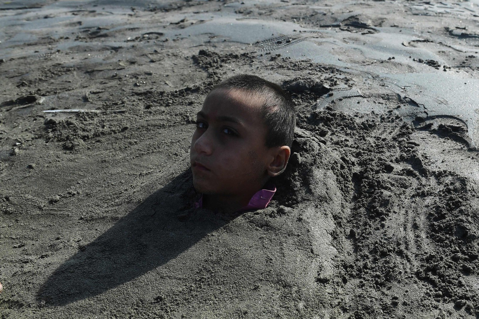 Menino é coberto de areia em uma praia por seus pais sob a crença de que a exposição durante um eclipse solar curará sua doença, em Karachi, Paquistão — Foto: ASIF HASSAN/AFP