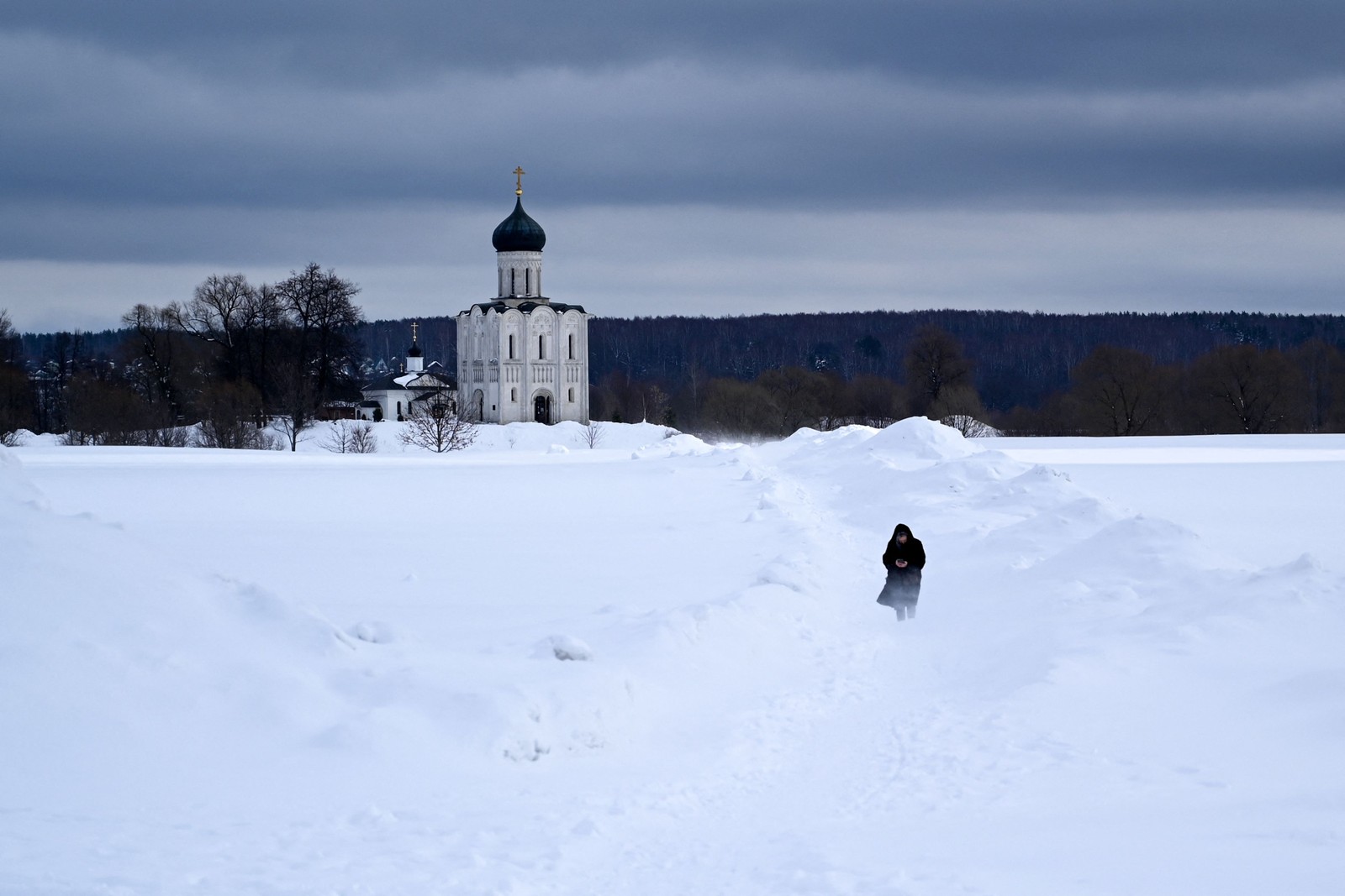 Mmulher caminha em um prado coberto de neve em frente ao Pokrova do século 12 na catedral ortodoxa de Nerli, fora da cidade de Vladimir, a cerca de 200 km de Moscou — Foto: KIRILL KUDRYAVTSEV/AFP