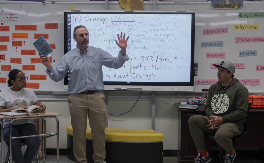 O professor de inglês Rick Ouimet segura um exemplar de “Wandering stars” de Tommy Orange (à dir.), durante palestra do autor na Millennium Art Academy, no Bronx