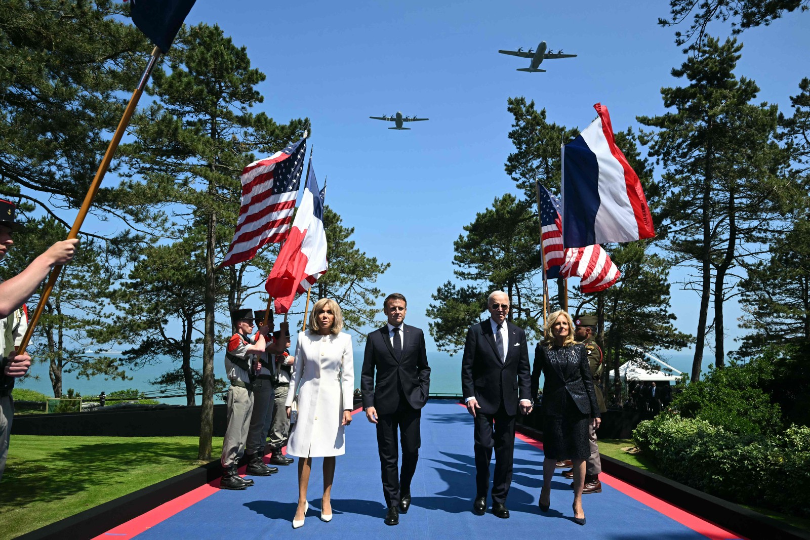 Aeronaves Douglas C-47 sobrevoam enquanto o presidente dos EUA Joe Biden (2º à direita), a primeira-dama dos EUA Jill Biden (direita), o presidente da França Emmanuel Macron (2º à esquerda) e sua esposa Brigitte Macron (esquerda) passam pelos porta-bandeiras durante a cerimônia dos EUA que marca o 80º aniversário do desembarque dos Aliados do "Dia D" da Segunda Guerra Mundial na Normandia, no Cemitério e Memorial Americano da Normandia em Colleville-sur-Mer, com vista para a Praia de Omaha. — Foto: SAUL LOEB / AFP