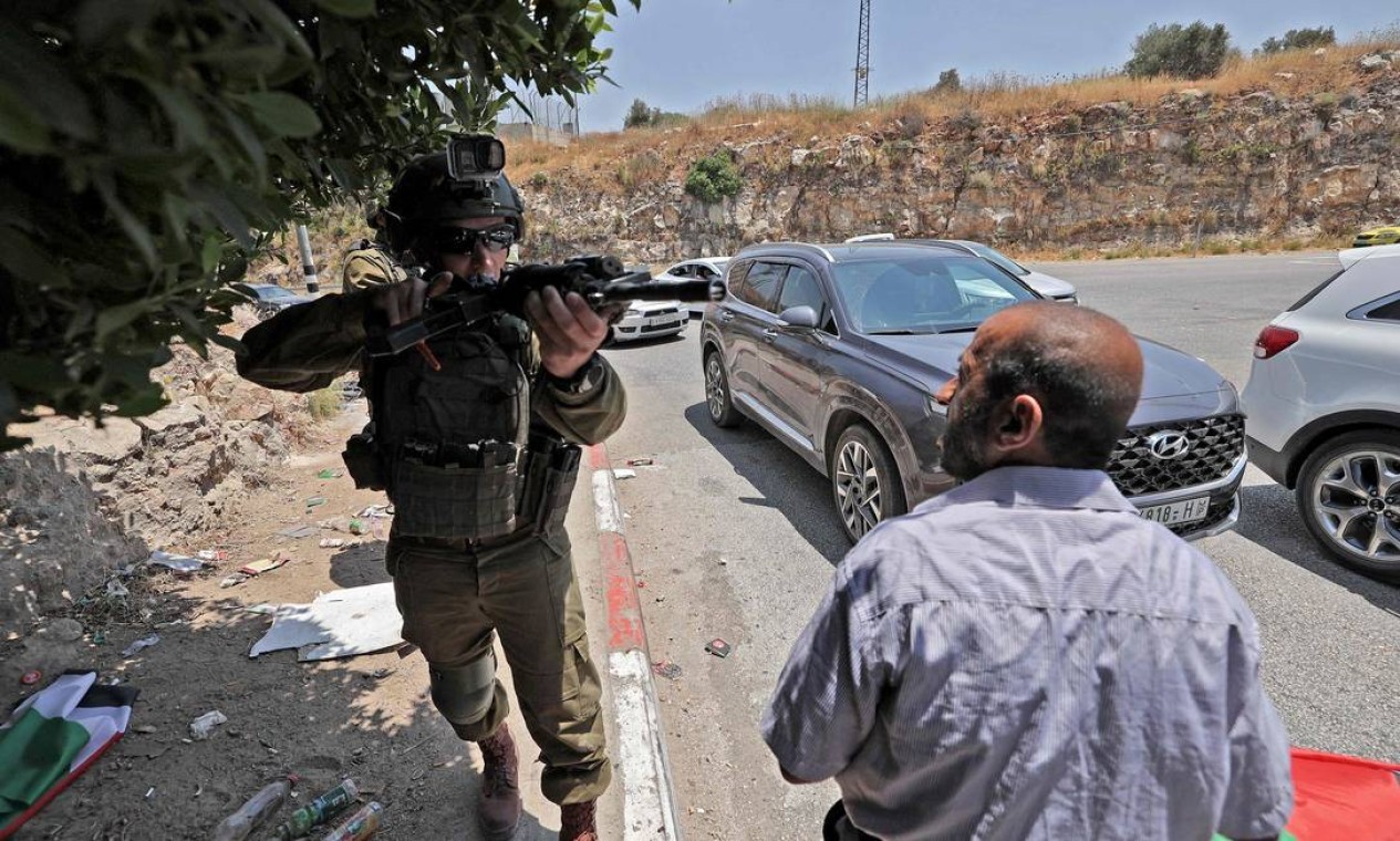 Soldado israelense interrompe o avanço de uma procissão fúnebre, de um homem palestino morto durante confrontos com as forças israelenses, em um posto de controle que sai da aldeia palestina de Nilin, a oeste de Ramallah, na Cisjordânia ocupada  — Foto: ABBAS MOMANI / AFP