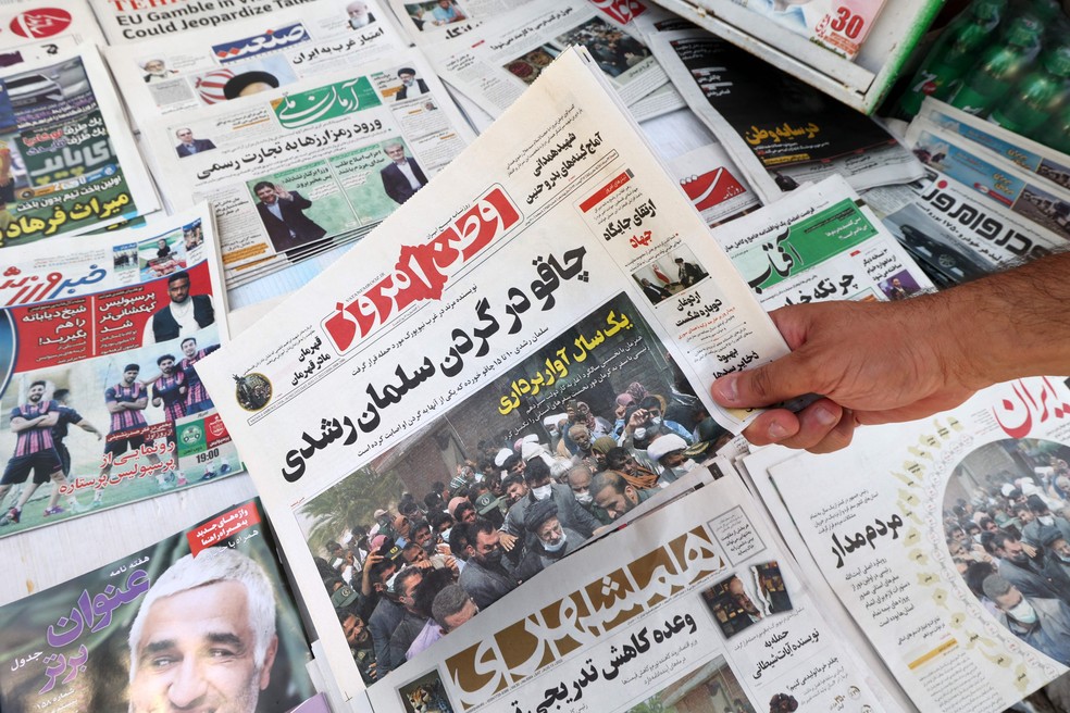 Um homem mostra a edição de jornais iranianos com o título da primeira página em farsi: "Faca no pescoço de Salman Rushdie" — Foto: AFP