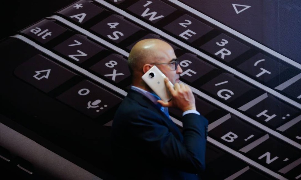 Homem fala ao celular enquanto passa em frente a um teclado do antigo Blackberry — Foto: Bloomberg