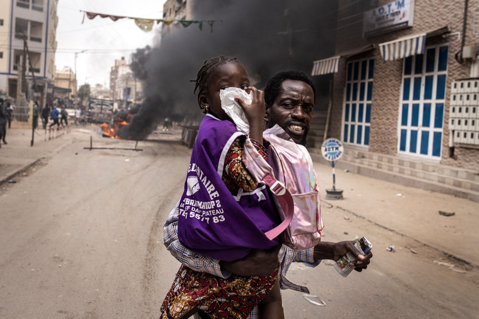 Homem corre com sua filha enquanto ela cobre o nariz do gás lacrimogêneo em Dacar, palco de protestos durante julgamento de líder da oposição preso — Foto: JOHN WESSELS/AFP