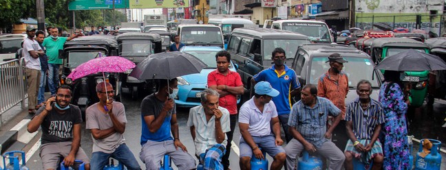 Pessoas sentadas em cilindros de gás vazios  bloqueiam estrada para protestar contra a escassez de combustível e gás de cozinha em Colombo, no Sri LankaAFP