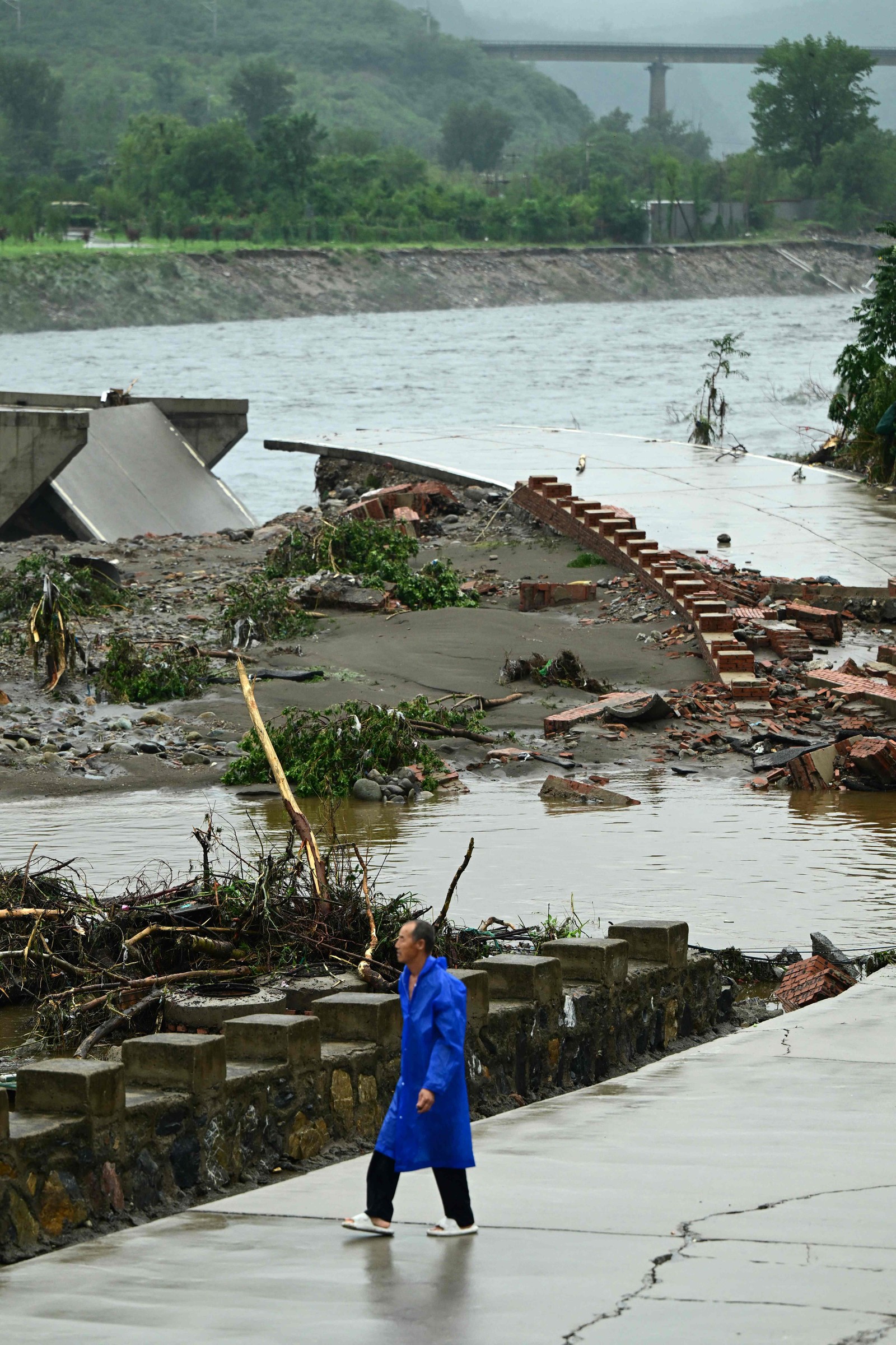 Um homem passa por uma ponte que desabou no rio Dashihe após fortes chuvas no distrito de Fangshan — Foto: Pedro PARDO / AFP