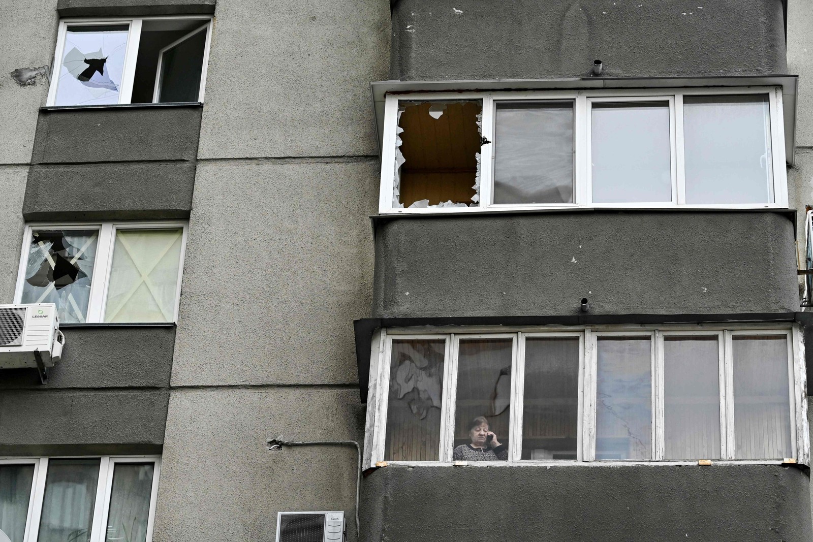 Morador olha pela varanda de um prédio residencial de vários andares com janelas danificadas por fragmentos de foguete russo em Kiev, Ucrânia — Foto: GENYA SAVILOV/AFP
